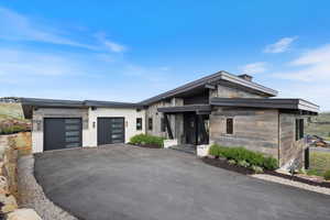 Contemporary home with stone siding, an attached garage, and asphalt driveway