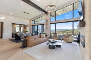 Living room featuring beamed ceiling, a towering ceiling, light wood finished floors, a glass covered fireplace, and recessed lighting