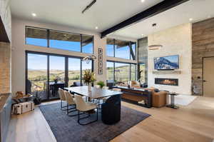 Dining area featuring a fireplace, light wood-type flooring, beam ceiling, a towering ceiling, and recessed lighting