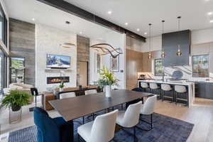 Dining space with a towering ceiling, a stone fireplace, light wood-type flooring, and recessed lighting