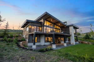 Back of property with a patio area, a balcony, a lawn, and stone siding