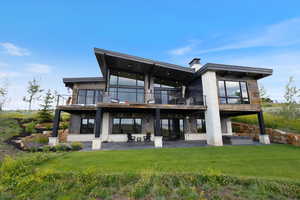 Rear view of house with a balcony, a patio area, a yard, and a chimney