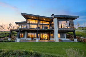 Back of property at dusk featuring a patio, a balcony, and a lawn