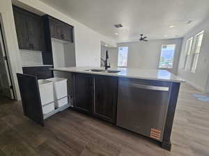 Kitchen featuring dishwasher, decorative backsplash, dark wood-style flooring, light stone counters, and an island with sink