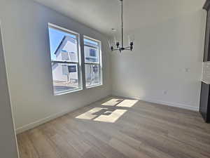 Unfurnished dining area featuring a chandelier and light wood-style flooring