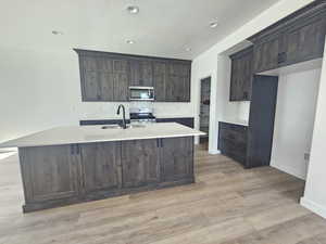 Kitchen featuring decorative backsplash, dark brown cabinetry, stainless steel appliances, a center island with sink, and light wood finished floors