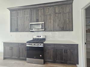 Kitchen featuring appliances with stainless steel finishes, decorative backsplash, and dark brown cabinetry