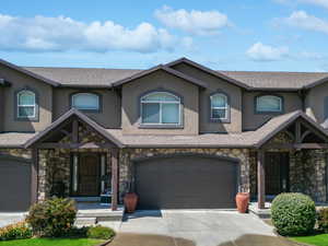 View of front of home featuring stucco siding, stone siding, driveway, roof with shingles, and a garage