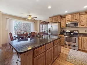 Kitchen featuring appliances with stainless steel finishes, dark stone counters, a breakfast bar area, light wood-style floors, and recessed lighting
