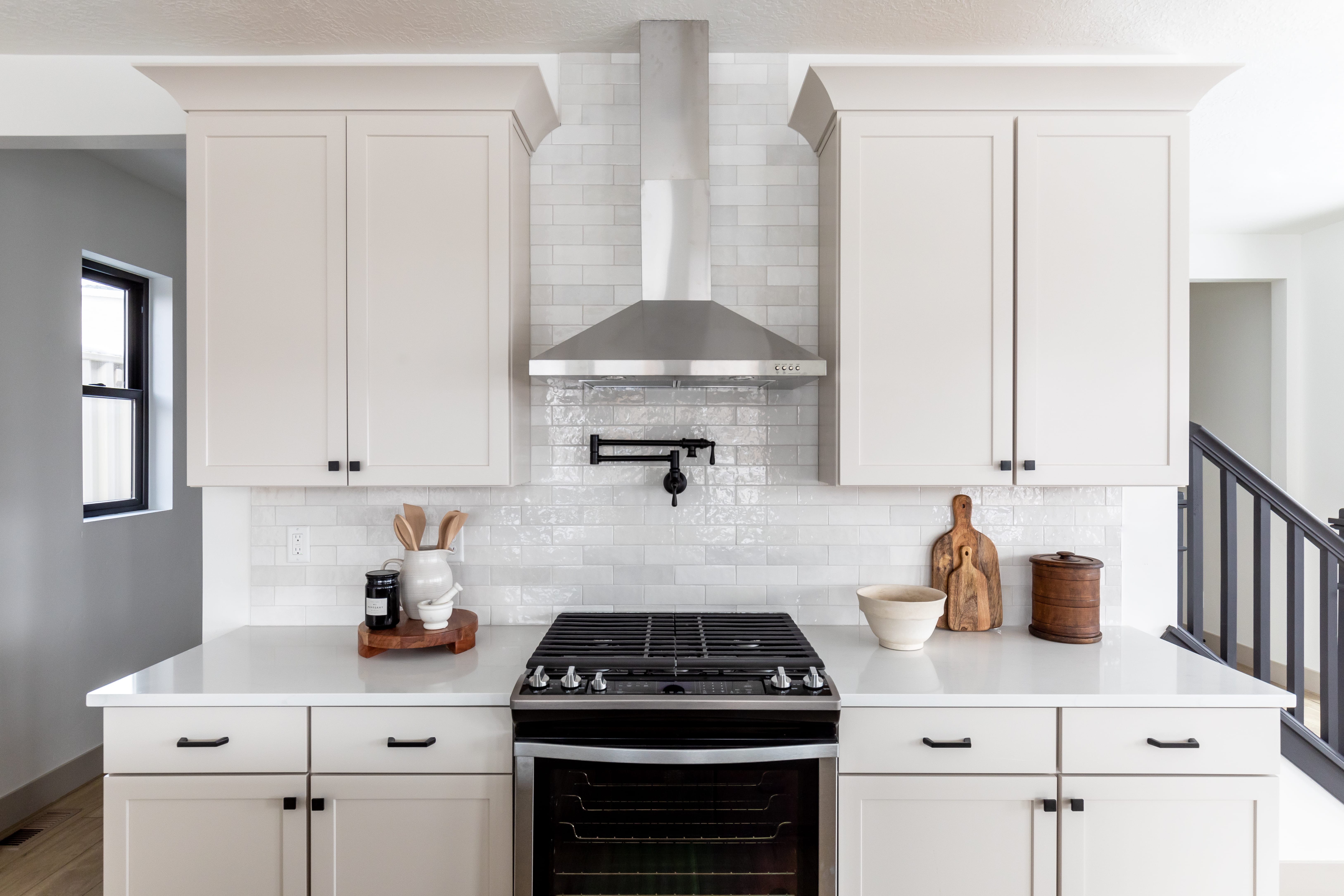 Kitchen featuring gas stove, wall chimney exhaust hood, decorative backsplash, and white cabinetry