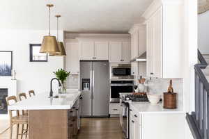 Kitchen featuring a breakfast bar, white cabinets, stainless steel appliances, and decorative light fixtures