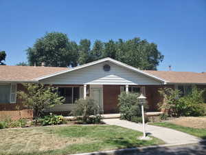 Ranch-style house featuring brick siding, covered porch, a front yard, and a shingled roof