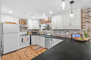 Kitchen with dark countertops, white appliances, white cabinets, light wood-style flooring, and brick wall