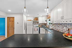 Kitchen with dark countertops, decorative light fixtures, a peninsula, white cabinetry, and recessed lighting