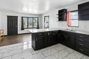 Kitchen featuring dark cabinets, decorative backsplash, healthy amount of natural light, a textured ceiling, and a peninsula
