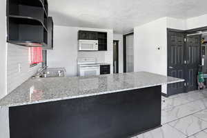 Kitchen featuring dark cabinetry, open shelves, decorative backsplash, white appliances, and a textured ceiling