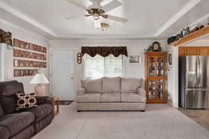 Family room area featuring a ceiling fan, carpet floors, and crown molding with tray ceiling.