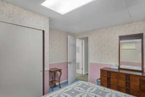 Bedroom featuring a drop ceiling, wallpapered walls, carpet flooring, and wainscoting
