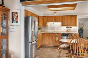 Kitchen featuring stainless steel fridge, crown molding, brown cabinets, and quartz countertops.