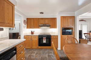 Kitchen with black & stainless steel appliances, ornamental molding, brown cabinetry, under cabinet range hood, under cabinet lighting and quartz countertops.
