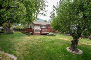View of green lawn featuring a deck around the back of the home.