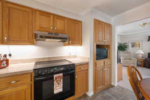 Kitchen featuring black electric range, crown molding, under cabinet range hood, under cabinet lighting, brown cabinets, and quartz countertops