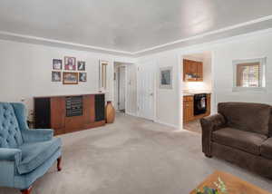 Living area with light colored carpet and crown molding.  View of the the hallway going towards bedrooms, and view of the entry into the kitchen.