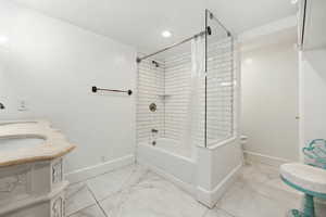 Bathroom featuring shower / bath combination with curtain, double vanity, light marble finish floors, and recessed lighting