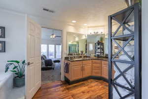 Ensuite bathroom featuring dark wood finished floors, a textured ceiling, vanity, a bath, and a ceiling fan