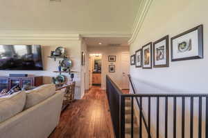 Corridor with an upstairs landing, a textured ceiling, dark wood-style floors, and crown molding