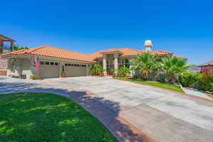 Mediterranean / spanish-style home with a tile roof, an attached garage, concrete driveway, stucco siding, and a front lawn