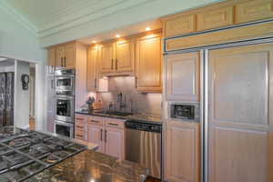 Kitchen with stainless steel appliances, dark stone countertops, backsplash, ornamental molding, and recessed lighting