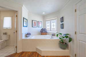 Full bath with wood finished floors, a textured ceiling, a garden tub, and crown molding