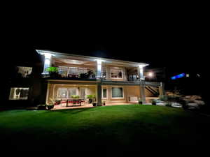 Back of house at twilight featuring a lawn, a patio, a balcony, and stairway