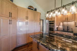 Kitchen featuring dark stone counters, dark wood-style floors, crown molding, decorative backsplash, and appliances with stainless steel finishes