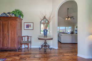 Sitting room with ceiling fan, dark wood-type flooring, ornamental molding, vaulted ceiling, and arched walkways