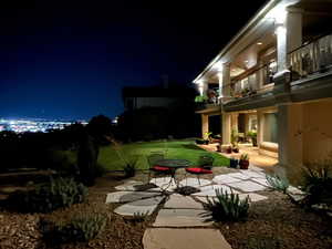 Yard at night featuring a balcony, a patio, and a lawn