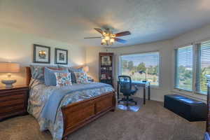 Carpeted bedroom featuring a textured ceiling, a ceiling fan, and an office area