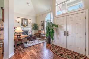 Foyer entrance featuring plenty of natural light, dark wood-style floors, crown molding, a high end fireplace, and lofted ceiling