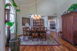 Dining room featuring dark wood-style flooring, ornamental molding, high vaulted ceiling, and a chandelier