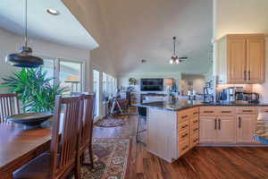 Kitchen with a peninsula, dark stone counters, a kitchen breakfast bar, light brown cabinets, and dark wood-style flooring