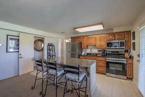 Kitchen with brown cabinetry, appliances with stainless steel finishes, a kitchen breakfast bar, a kitchen island, and dark stone counters