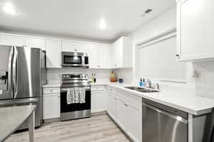 Kitchen with appliances with stainless steel finishes, light wood-type flooring, white cabinetry, and light stone countertops