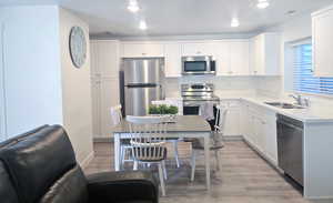 Kitchen with stainless steel appliances, white cabinets, light wood finished floors, light stone counters, and recessed lighting