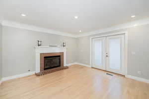 Family room featuring ornamental molding, light wood-style flooring, french doors, a brick fireplace, and recessed lighting