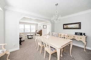 Dining space featuring arched walkways, crown molding, carpet floors, a textured ceiling, and a chandelier