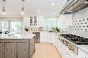 Kitchen featuring glass insert cabinets, light stone countertops, appliances with stainless steel finishes, white cabinets, and recessed lighting