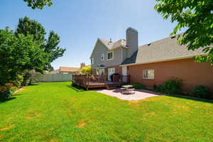 Back of house featuring a wooden deck, a patio, a shingled roof, a chimney, and brick siding