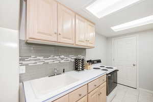 Kitchen featuring light brown cabinets, white electric range, backsplash, light countertops, and light tile patterned floors