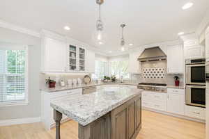 Kitchen with white cabinetry, light stone counters, glass insert cabinets, light wood finished floors, and backsplash
